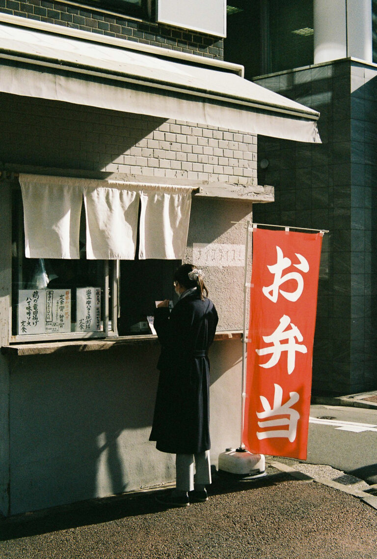 A person standing at a bento shop in sunlight.