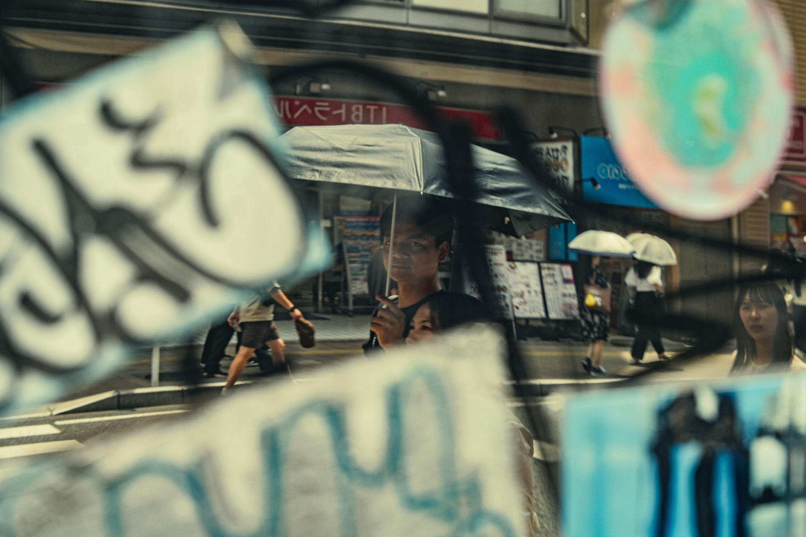 A rainy street seen through a shop window layered with handwritten signs and reflections — Surfaces