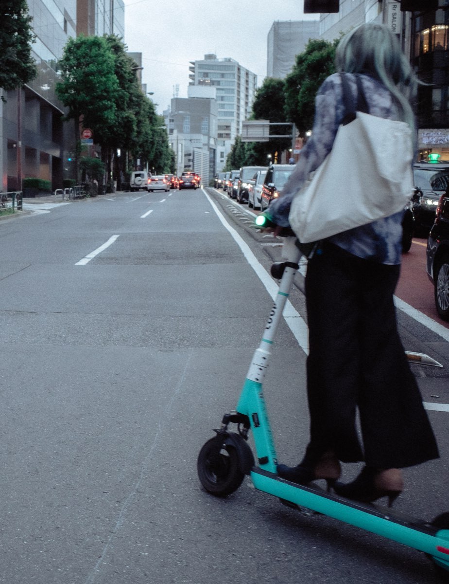A woman riding a green electric scooter through the city.